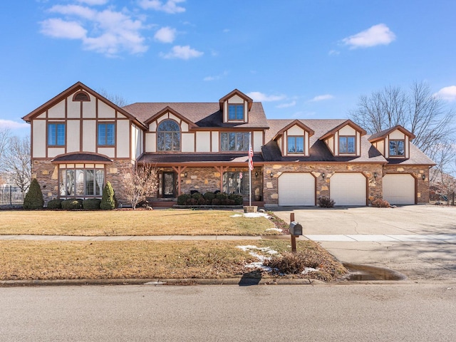 tudor house with an attached garage, a shingled roof, driveway, stone siding, and a front yard