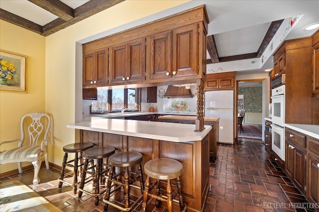 kitchen with a peninsula, white appliances, baseboards, and light countertops