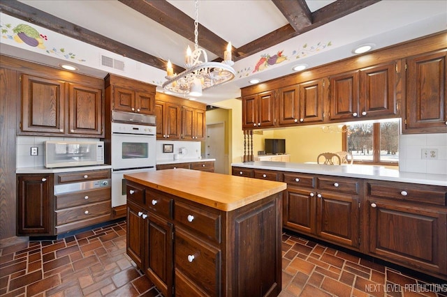 kitchen with white appliances, visible vents, decorative backsplash, a chandelier, and beam ceiling