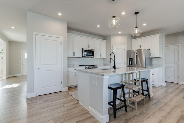 kitchen featuring appliances with stainless steel finishes, an island with sink, sink, white cabinets, and light stone counters