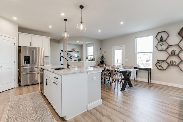 kitchen featuring sink, a center island with sink, appliances with stainless steel finishes, light stone countertops, and white cabinets