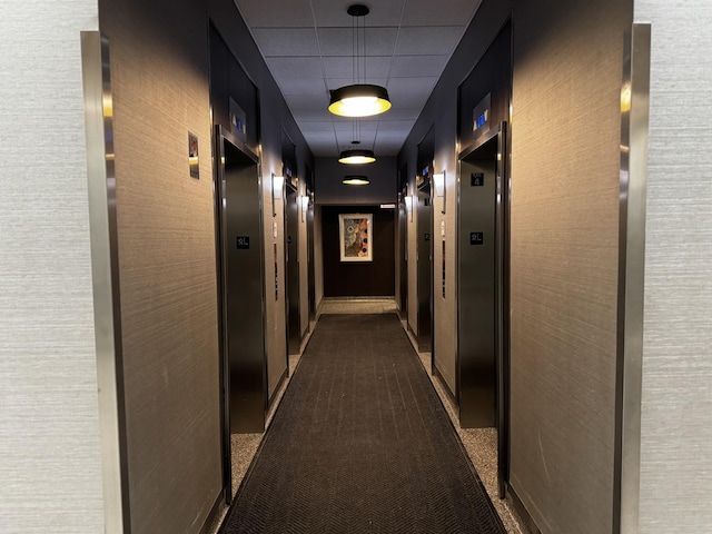 hall featuring a paneled ceiling and dark carpet