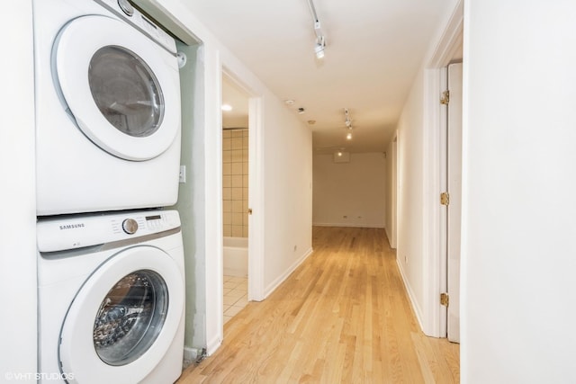 laundry area featuring stacked washer and dryer, track lighting, and light hardwood / wood-style floors