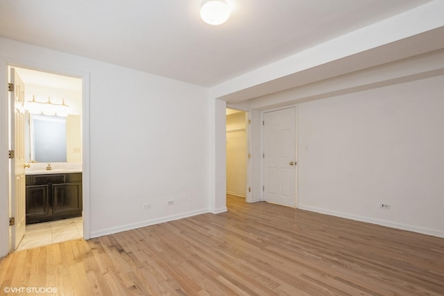 unfurnished bedroom with ensuite bathroom, sink, a closet, and light wood-type flooring