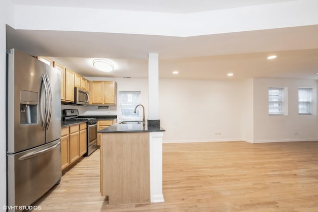 kitchen featuring sink, light brown cabinets, light hardwood / wood-style floors, stainless steel appliances, and a center island with sink