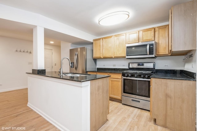 kitchen with light brown cabinetry, sink, dark stone counters, stainless steel appliances, and light hardwood / wood-style floors