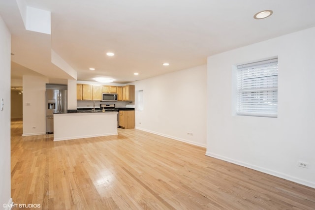 kitchen featuring sink, appliances with stainless steel finishes, a kitchen island with sink, light brown cabinets, and light wood-type flooring