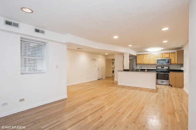 kitchen featuring stacked washing maching and dryer, appliances with stainless steel finishes, sink, and light wood-type flooring