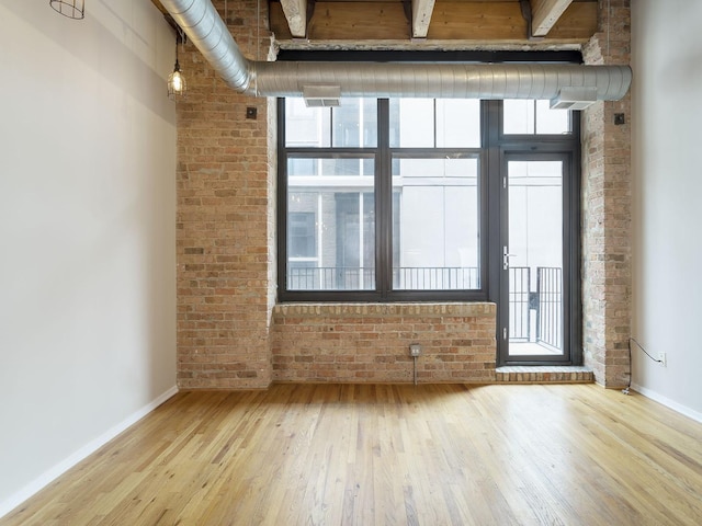 empty room with plenty of natural light, wood-type flooring, and brick wall