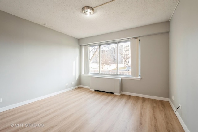 empty room with radiator heating unit, light hardwood / wood-style floors, and a textured ceiling