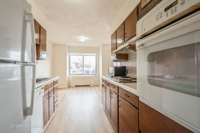 kitchen featuring a textured ceiling, radiator, white appliances, light hardwood / wood-style floors, and decorative backsplash