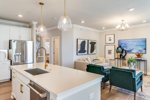 kitchen featuring sink, hanging light fixtures, stainless steel appliances, white cabinets, and a center island with sink