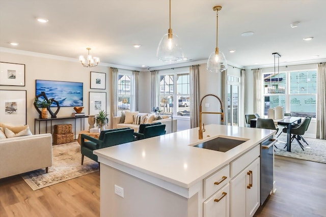 kitchen with pendant lighting, sink, ornamental molding, an island with sink, and white cabinets