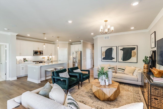 living room featuring an inviting chandelier, sink, ornamental molding, and light hardwood / wood-style floors