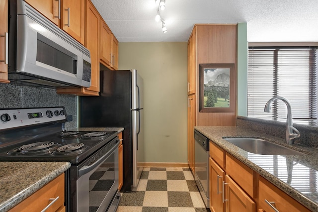 kitchen with stainless steel appliances, sink, a textured ceiling, and dark stone counters