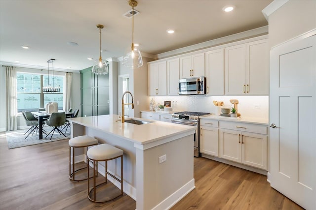 kitchen with a kitchen island with sink, sink, white cabinetry, and appliances with stainless steel finishes