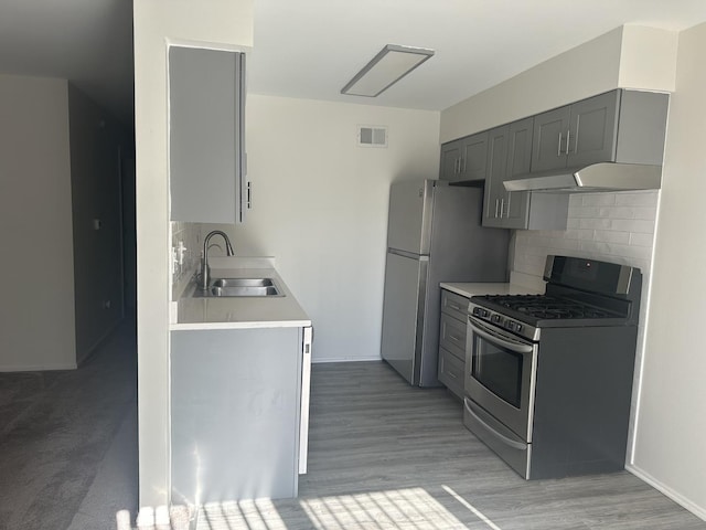 kitchen with under cabinet range hood, stainless steel appliances, a sink, light countertops, and gray cabinets