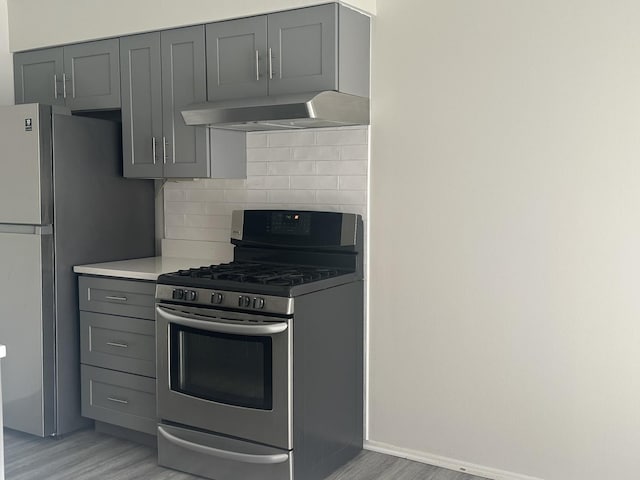 kitchen with stainless steel appliances, tasteful backsplash, gray cabinets, light countertops, and extractor fan