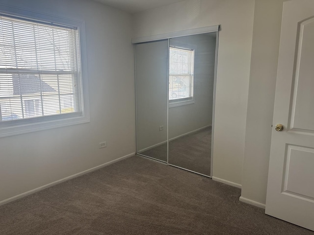 unfurnished bedroom with baseboards, multiple windows, dark carpet, and a closet