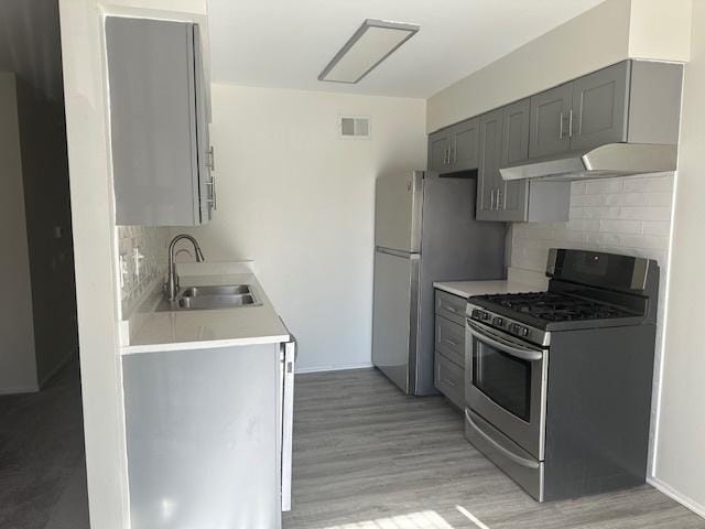 kitchen with appliances with stainless steel finishes, light countertops, gray cabinetry, under cabinet range hood, and a sink