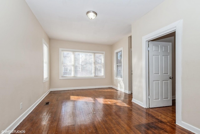 unfurnished room featuring visible vents, baseboards, and dark wood-type flooring