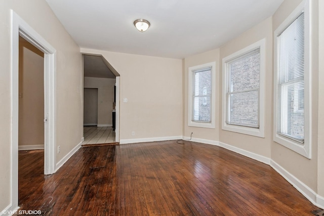 unfurnished room with baseboards, arched walkways, and dark wood-style flooring