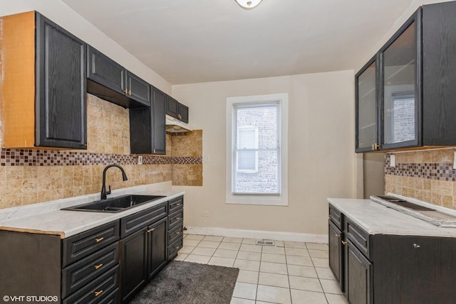 kitchen featuring light tile patterned floors, baseboards, glass insert cabinets, light countertops, and a sink