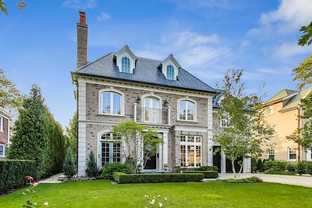 georgian-style home featuring a balcony, brick siding, driveway, a front lawn, and a high end roof