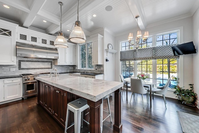 kitchen with white cabinets, beam ceiling, stainless steel stove, and range hood