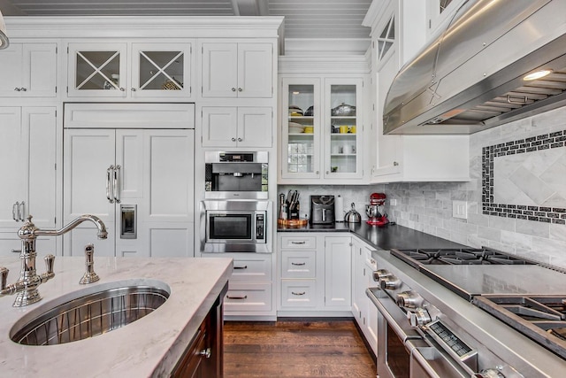 kitchen featuring white cabinetry, a sink, under cabinet range hood, and built in appliances