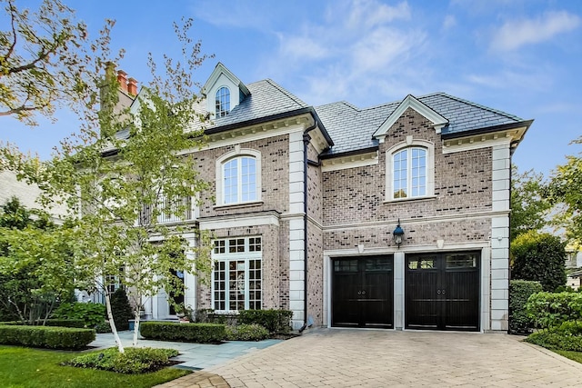 view of front facade featuring a garage, a high end roof, decorative driveway, and brick siding