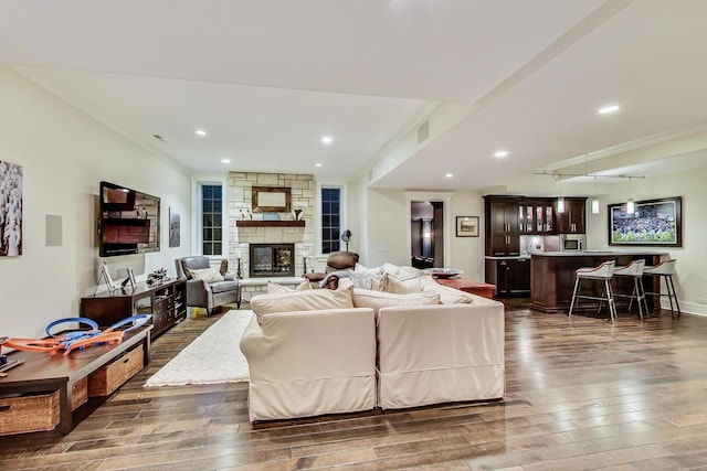 living room with a stone fireplace, indoor bar, dark wood-style flooring, and visible vents