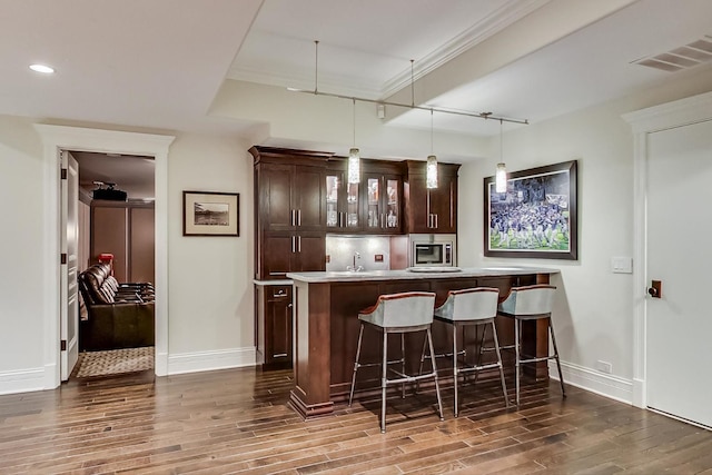 bar with visible vents, dark wood-style floors, stainless steel microwave, hanging light fixtures, and wet bar