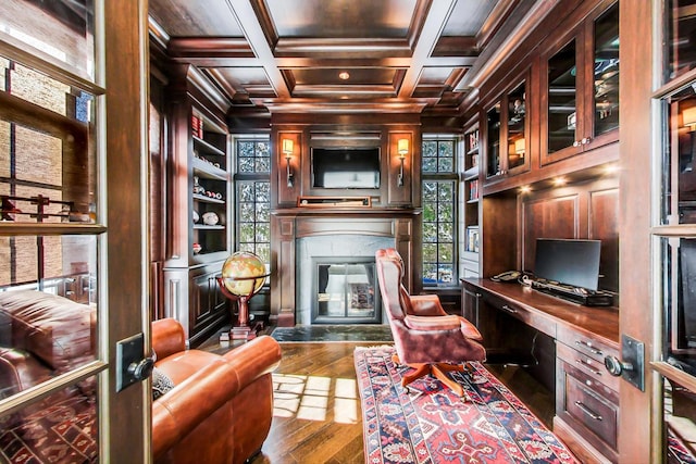 office area with coffered ceiling, a glass covered fireplace, built in study area, hardwood / wood-style floors, and built in shelves