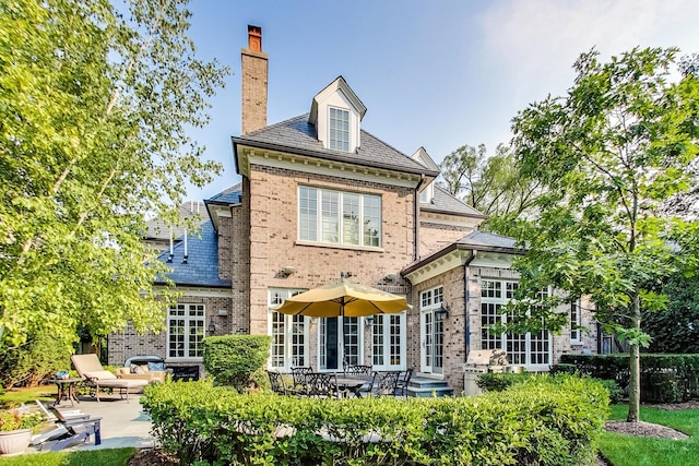 rear view of house with entry steps, brick siding, a chimney, a patio area, and a high end roof