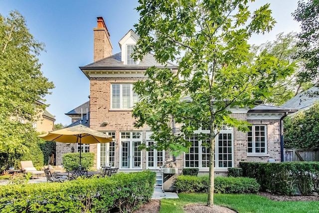 rear view of house with french doors, brick siding, a chimney, and a patio