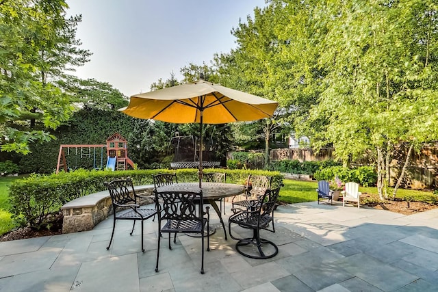 view of patio featuring fence, outdoor dining area, and a playground