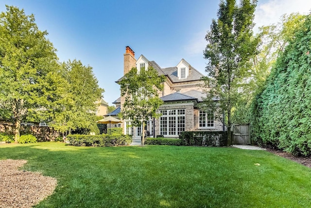 back of house featuring a yard, a chimney, and a gate