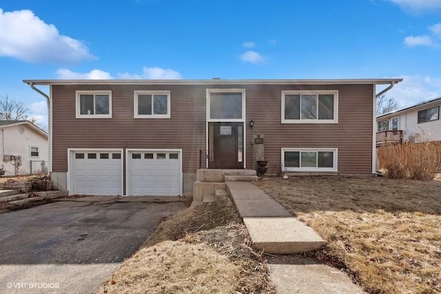 bi-level home with aphalt driveway, an attached garage, and fence