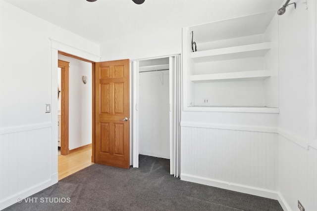 unfurnished bedroom featuring a wainscoted wall, a closet, and dark carpet