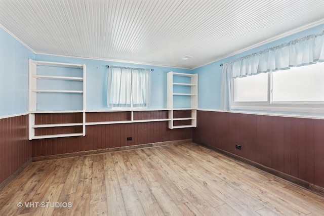 empty room with hardwood / wood-style flooring, wooden walls, ornamental molding, and a wainscoted wall