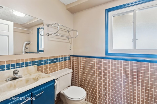 bathroom with wainscoting, toilet, a textured ceiling, vanity, and tile walls