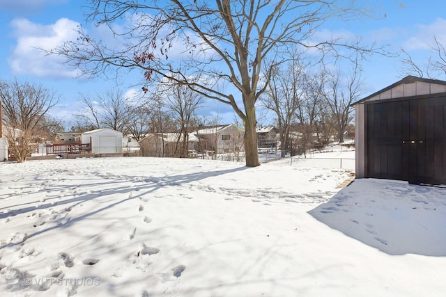 yard layered in snow featuring a garage, a shed, a deck, and an outdoor structure