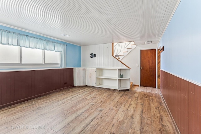 empty room featuring hardwood / wood-style flooring, a wainscoted wall, wood walls, stairs, and crown molding