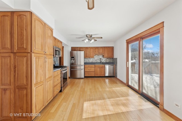 kitchen featuring light wood finished floors, ceiling fan, appliances with stainless steel finishes, backsplash, and a sink