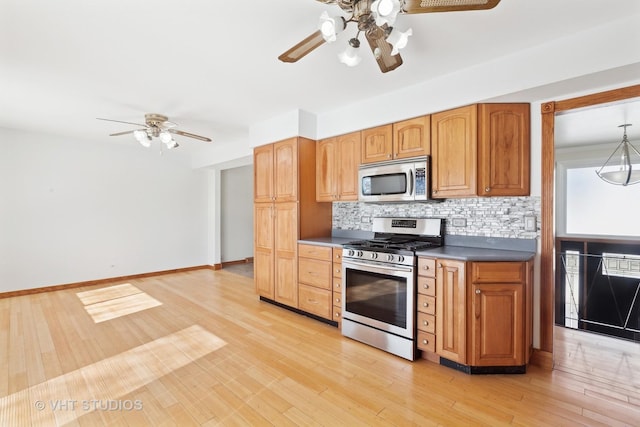 kitchen with light wood finished floors, appliances with stainless steel finishes, backsplash, and baseboards