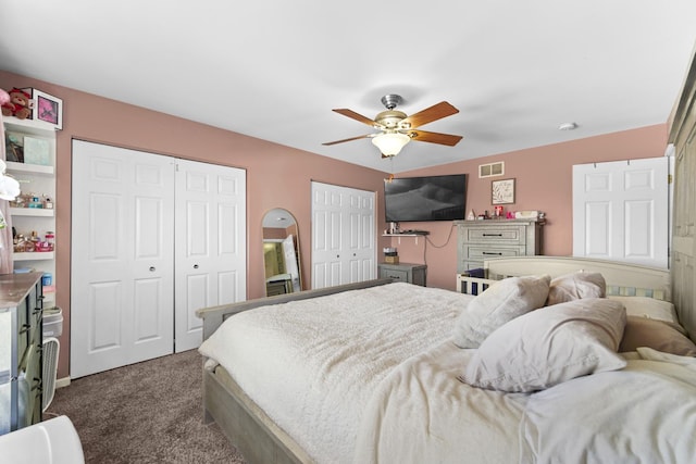 bedroom with a ceiling fan, visible vents, dark carpet, and two closets