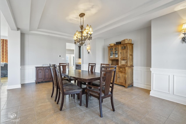 dining room with a chandelier, light tile patterned flooring, a decorative wall, wainscoting, and a raised ceiling