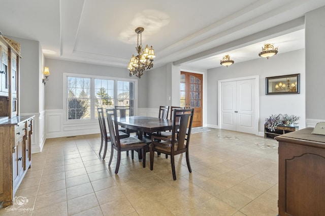 dining room with light tile patterned floors, a decorative wall, a wainscoted wall, a notable chandelier, and a raised ceiling