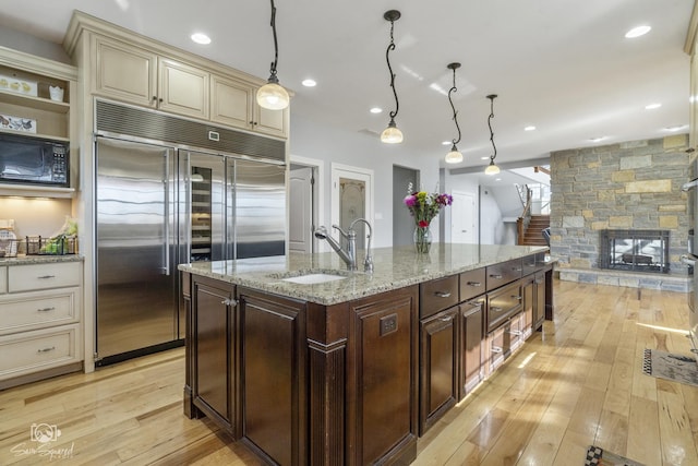 kitchen with black microwave, built in refrigerator, a sink, cream cabinetry, and light wood-type flooring